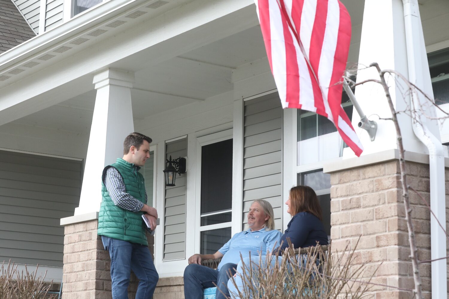 Andrew Ireland listening to residents on their front porch beneath an American flag